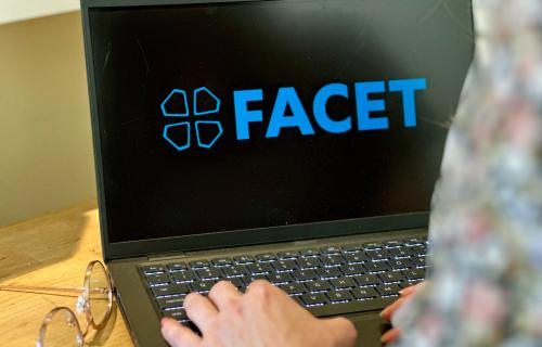 A laptop with the FACET logo on a desk.